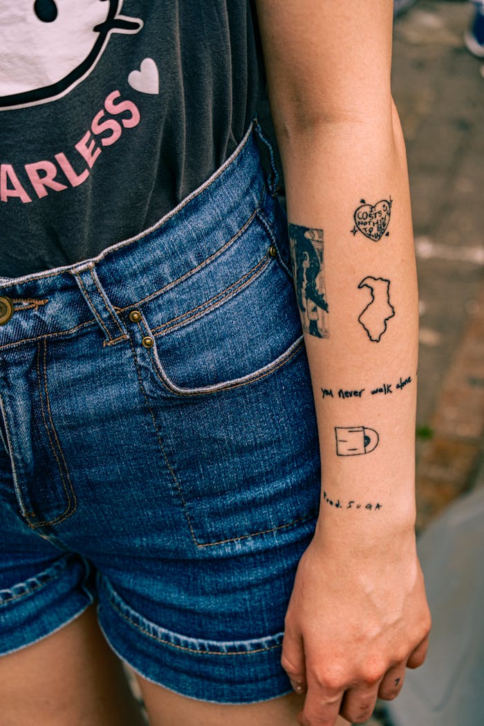 A woman's arm with various minimalist tattoos and denim shorts.