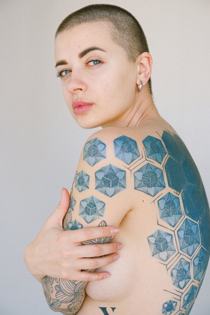 Tattooed woman posing in soft lighting, showcasing intricate geometric body art.