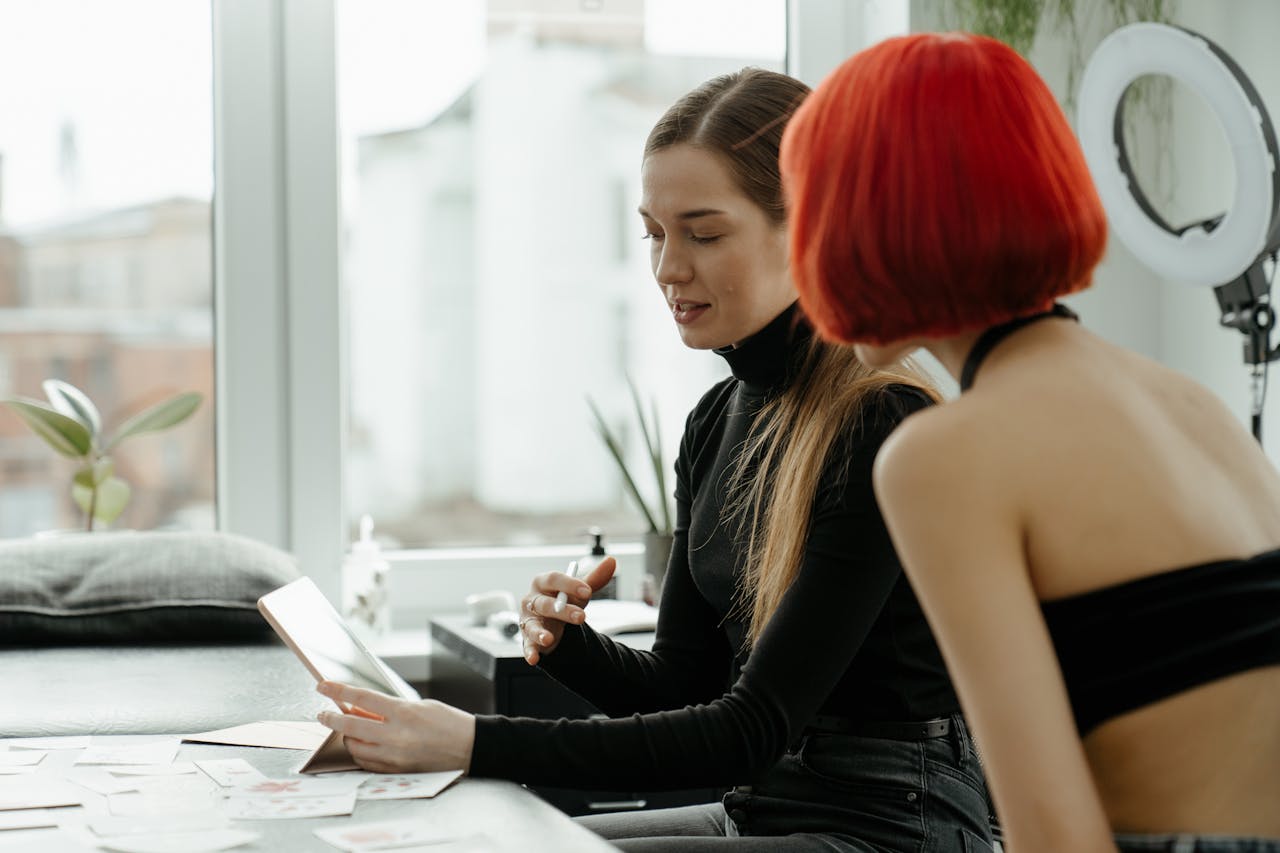 Two women discussing ideas in a creative tattoo studio with an artistic vibe and natural lighting.