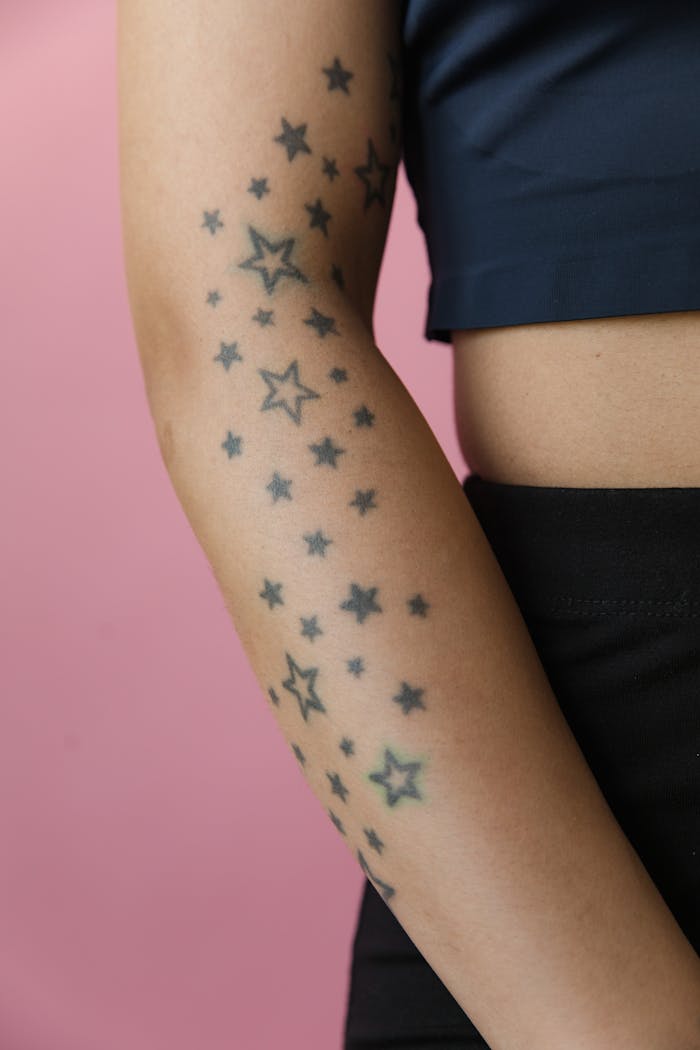 A close-up photo of an arm with star tattoos against a pink backdrop.